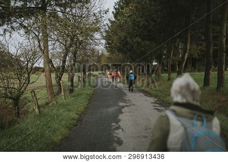 Sarria, Spain - April 7th, 2019: Camino De Santiago Pilgrims Walking With A Backpack Across A Rural 