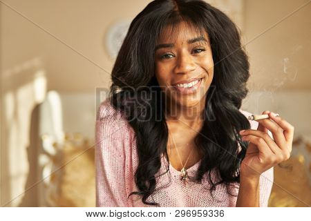 portrait of happy african american woman smoking pre-roll marijuana joint