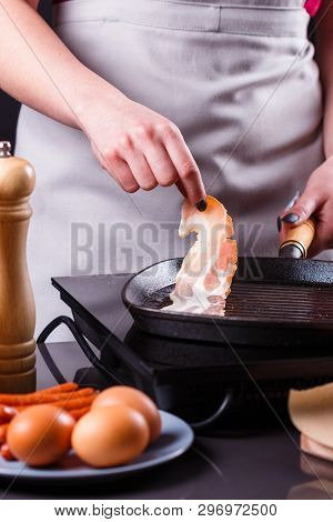 Young Woman In A Gray Apron Fries Bacon