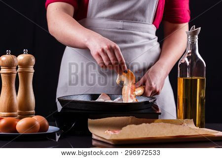 Young Woman In A Gray Apron Fries Bacon