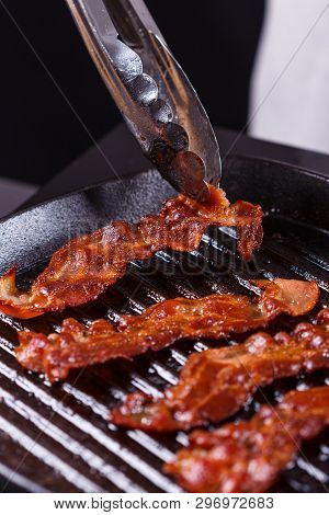 Young Woman In A Gray Apron Fries Bacon