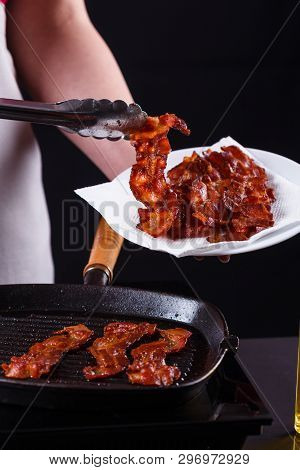 Young Woman In A Gray Apron Fries Bacon