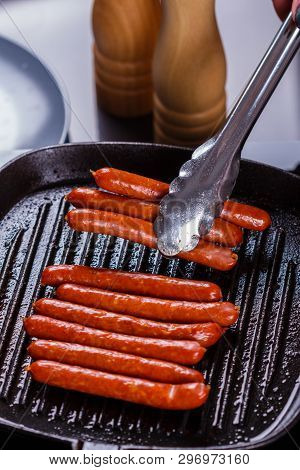 Young Woman In A Gray Apron Fries Sausages