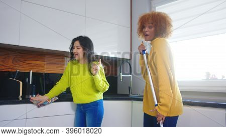 Best Friends Roommates Having Fun While Cleaning Kitchen. Singing And Dancing With Mop. High Quality