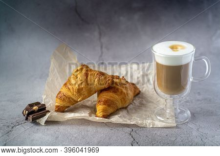 On A Gray Table There Is A Glass Cup With Hot Latte Coffee And Next To It.two Croissants Lie On A Gr