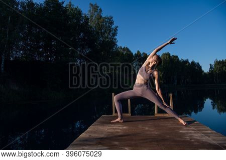 Young Woman Relaxing By The Lake At Sunset, Harms Outstretched. Doing Youga In The Morning At Forest
