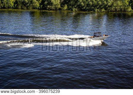 Speedboat Towing An Athlete On A Board Against The Background Of The Forest. Athlete Water Skiing An