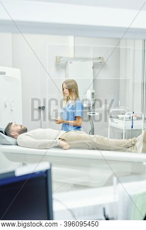 Young blond female doctor in medical uniform standing by bearded male patient lying on couchette during ultra sound examination in clinics