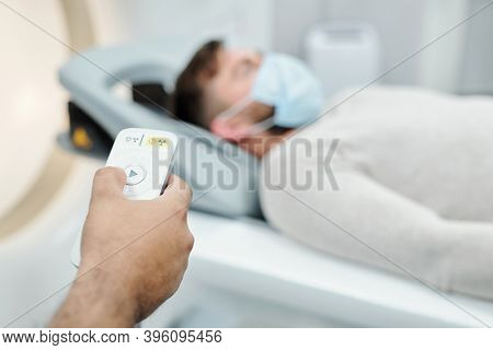 Hand of young male touching button on control panel while standing in front of patient on long couchette before medical examination