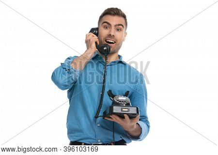 happily surprised casual man talking on an old telephone against white background