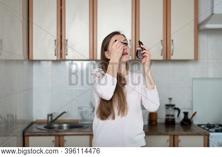 Girl Doing Make Up In Kitchen And Looking In Small Mirror.
