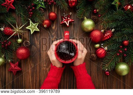 Woman Holding Hot Christmas Tea With Santas Sleigh And Deers Reflection Against Decorations On Woode