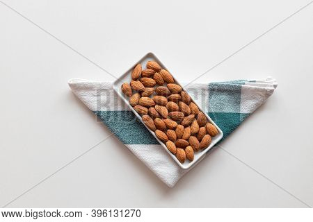 Creative Layout Made Of Fresh Nut Almonds In A Ceramic Bowl With A Towel On A White Background. Flat