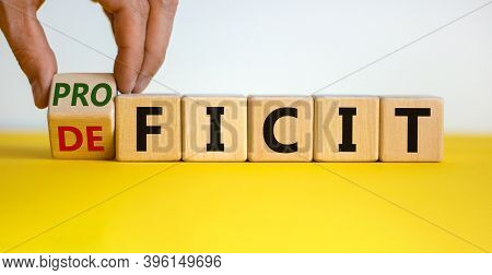 Deficit Or Proficit. Hand Turns A Cube And Changes The Word 'deficit' To 'proficit' Or Vice Versa. B