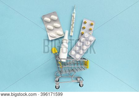 Shopping Grocery Cart With Medicament, Tablet, Spray, Thermometer On Blue Background. Concept Of Hea