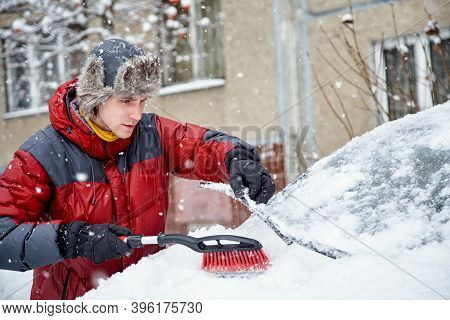 A Man Brushing The Snow Off The Windshield Of His Car