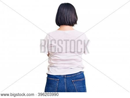 Brunette woman with down syndrome wearing casual white tshirt standing backwards looking away with crossed arms 