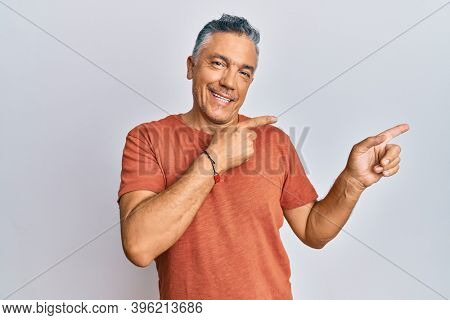 Handsome middle age mature man wearing casual clothes smiling and looking at the camera pointing with two hands and fingers to the side. 