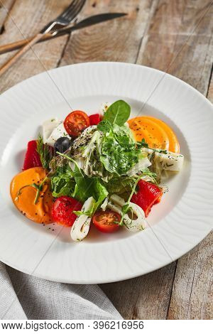 Roasted pepper salad with calamari and fresh greens. Rustic wooden table and grey textile