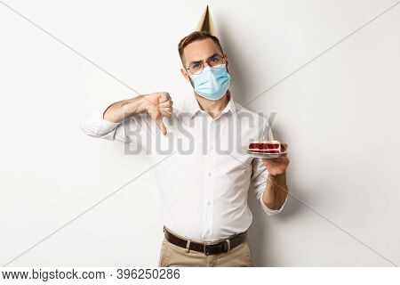 Covid-19, Social Distancing And Celebration. Disappointed Birthday Guy Wearing Face Mask, Holding Bd