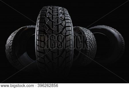 Stack Of Four New Black Tyres For Winter Car On Black Background
