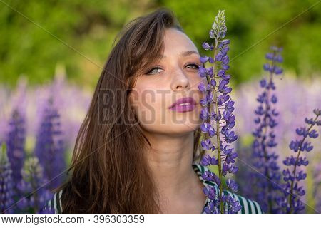 Gorgeous Beautiful Girl Leans Face Against Lupin Flower Sensually Looking At Camera On Blooming Mead