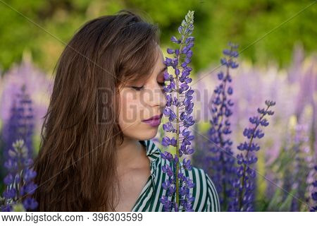 Gorgeous Beautiful Girl Eyes Closed Leans Head Against Lupin Flower On Blooming Meadow, Merging With