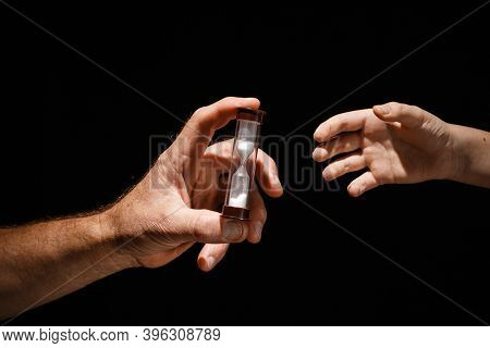 Adalt Hand Passes The Glass Hourglass To The Child Concept Of The Generation Change On A Black Isola