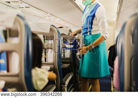 Flight Attendant In Facial Mask Protection From Covid-19 Serves Passengers A Coffee.