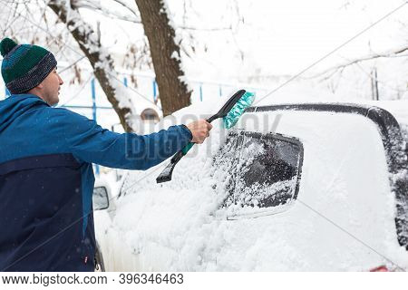 A Man Brushes Snow From A Car After A Snowfall. A Hand In A Blue Jacket With A Car Broom On The Whit