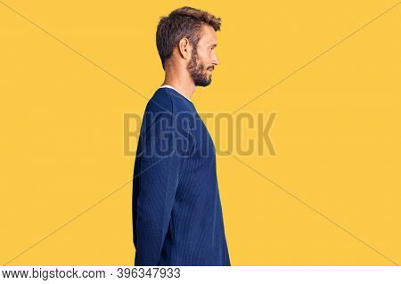 Handsome blond man with beard wearing casual sweater looking to side, relax profile pose with natural face and confident smile. 
