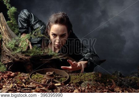 A Young Woman In A Black Leather Jacket Climbs Out Of The Pit Holding On To A Snag. Angry Girl Stret