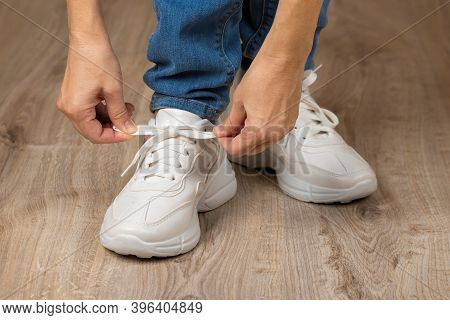 Caucasian Woman Hands Tie Elastic Laces On Chunky Sole White Sneakers Shod On Her Feet On The Brown 