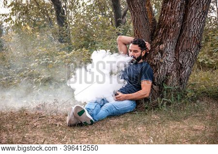 Stylish Bearded Smoker Blows Up A Couple An Electronic Cigarette Outside. Modern Ways Of Quitting To