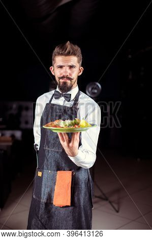 Young Steward Helpfully Holds Plate With Prepared Dish At A Festive Event.
