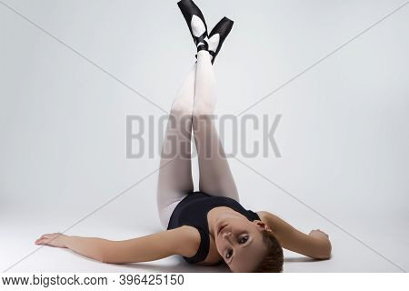 Portrait Of Caucasian Ballet Dancer In Body Suit And Pointes Shoes Lying On Back Against White Backg