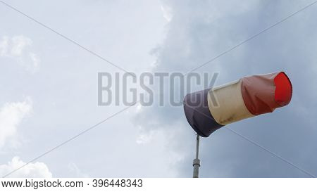 Flying Windsock Wind Vane With Red, White And Blue Lines On Dramatic Sky Background. Test Wind Direc