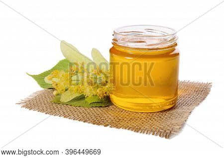 Open Jar Of Linden Honey And Lime Flowers Isolated On White Background.