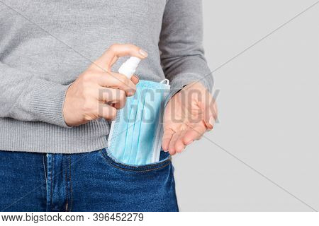 Hand With Medicine Protective Mask And Anticeptic In Jeans Pocket On Grey Background.