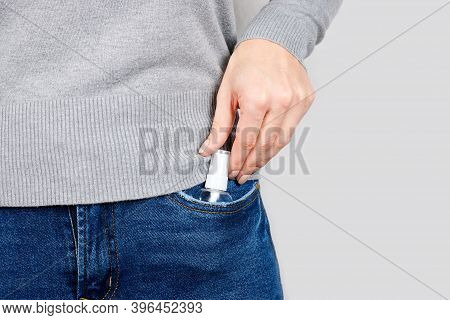 Hand With Medicine Anticeptic In Jeans Pocket On Grey Background.