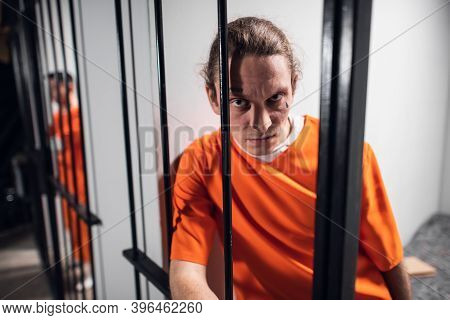 Psychological Portrait Of An Evil And Wild Prisoner Through The Bars Of A Prison Cell. A Strong Look