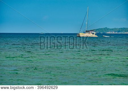 Philippines, Boracay Island, Puka Beach. A White Yacht Is Moored In The Sea With A White Rubber Boat
