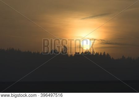 Telephoto Sunset Over A Distant Coniferous Forest At Redmires Reservoirs Near Sheffield. Hazy Sky As