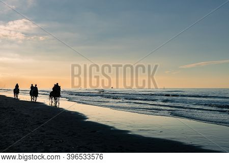 Koksijde, Belgium - November 5, 2020: Silhouetted Horseback Riders On The Beach At Sunset