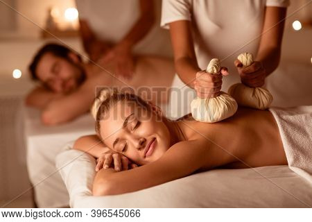 Couple Receiving Exotic Thai Herbal Massage With Aromatic Bags Enjoying And Relaxing Lying At Luxury