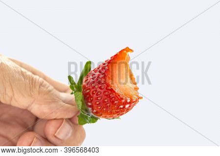 Bitten Off Red Strawberry With Green Leaves In Hand Against White Background
