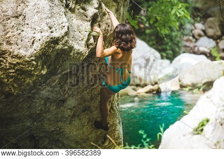 A Woman In A Swimsuit Climbs A Cliff Above The Water, Climbing Over A Mountain River, Bouldering In 