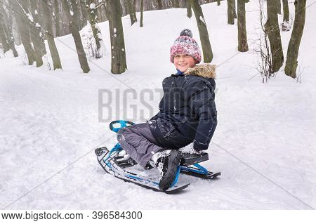 A Happy Boy In The Snow Is Sitting On A Snowcar In The Park.