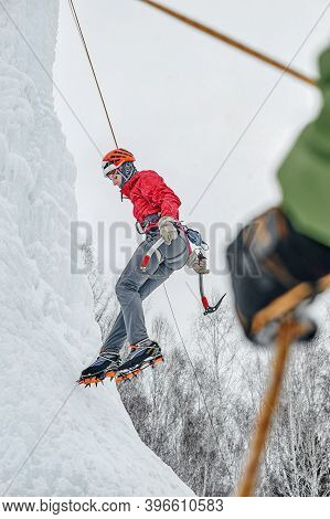 Alpinist Woman With Ice Tools Axe In Orange Helmet Climbing A L