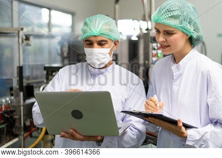 Quality Control Engineer Holds Computer To Work With Female Worker. Workers In The Factory Write Dow